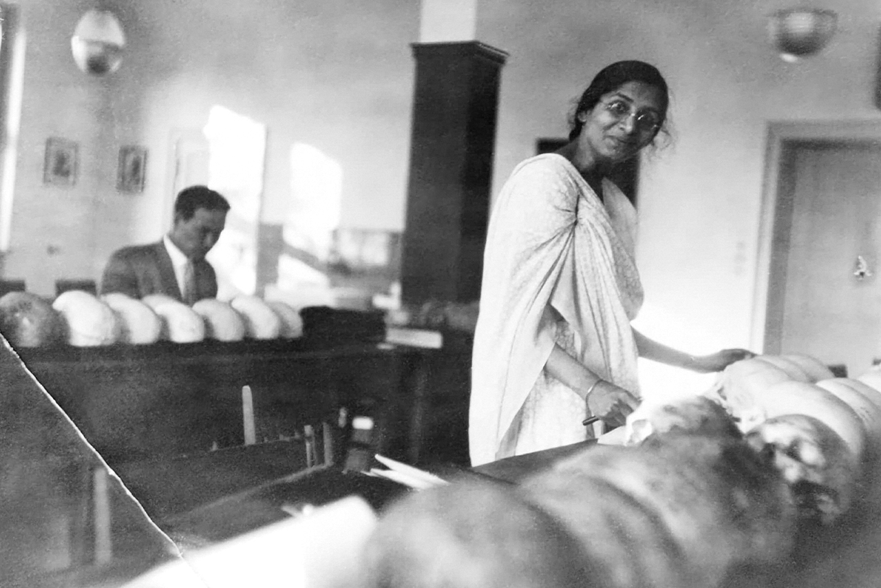 The second image is a photograph of a woman with dark skin, doctoral candidate Irawati Karvé. She is standing next to a table with a row of skulls.