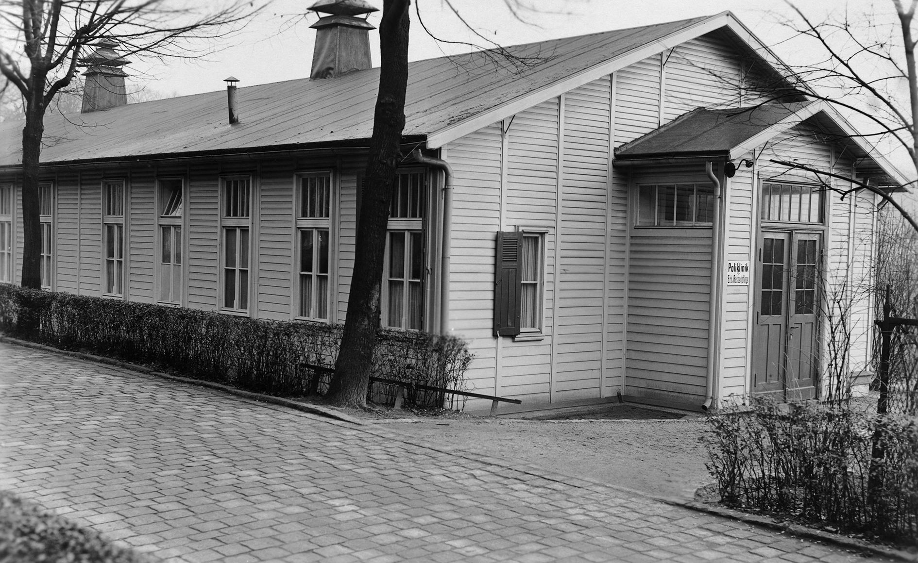 Photographs of the so-called Polyclinic for Hereditary and Racial Hygiene. The first is an exterior view of a one-story building with light-colored wooden walls.